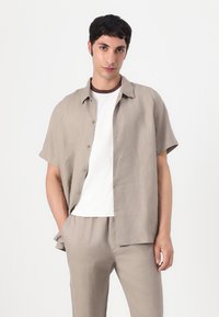 Short-sleeve, light beige linen shirt with button front, paired with a white T-shirt and matching pants. Smooth texture, relaxed fit.