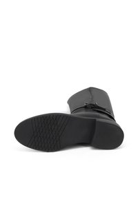 Stivale in pelle nera con tacco a blocco basso, superficie liscia e suola in gomma testurizzata che presenta un motivo a croce. Dettaglio della fibbia laterale visibile.