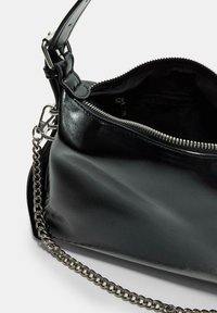 Sac à main en cuir noir avec une texture lisse, doté d'une fermeture éclair et d'une bandoulière en chaîne argentée. L'intérieur présente une doublure noire avec une petite poche.