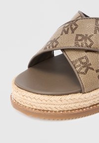 Sandale platformă maro din material împletit, cu barete încrucișate, talpă interioară netedă și mijloc de talpă învelit în iută. Partea inferioară are mici tăvi decorative.