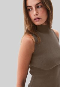 Bruine mouwloze top met een hoge hals en geribbelde textuur, met een aansluitend ontwerp en subtiele zijdetails.