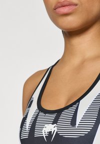 Top desportivo preto com desenho gráfico branco em contraste, apresentando corte nadador e faixa texturizada ao redor do decote.