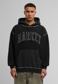 Svart hettegenser med "MARKET" trykt i hvitt, med frontlomme, snøring i hetten og kontrasterende sømdetaljer.