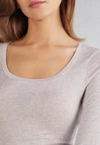 Hellgraues langärmliges Oberteil mit Rundhalsausschnitt, weichem Material und subtilen Melangé-Muster; figurbetonte Silhouette, die sich an den Körper anschmiegt.