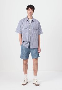 Kratek rokav srajca z gumbi v modro-belih karo vzorcih, z dvema žepoma na prsih, v kombinaciji z jeans kratkimi hlačami in belimi supergami.