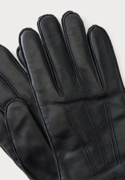 Paire de gants en cuir noir avec des surpiqûres visibles au dos, posés à plat sur un fond clair.