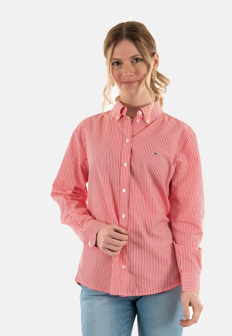 Camisa a rayas rojas y blancas con cuello clásico, mangas largas y un pequeño logo en el pecho. Textura de tela suave.