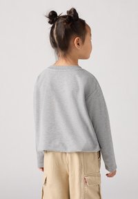 Sudadera gris de manga larga con cuello redondo, ajuste relajado y puños acanalados, combinada con pantalones cargo beige que tienen bolsillos laterales.