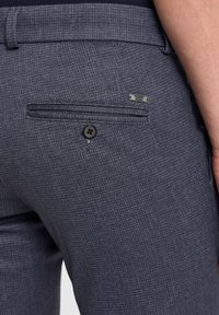 Dunkelgraue, strukturierte Hose mit einer Gesäßtasche mit einem schwarzen Knopf und einem kleinen Metall-Logo-Schild. Entworfen für eine taillierte Passform.