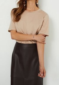 Béžový top s krátkým rukávem a volným střihem v kombinaci s přiléhavou tmavě hnědou koženou sukní. Vyznačuje se hladkými texturami a jednoduchým designem.