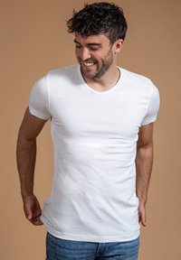 Witte V-hals t-shirt gemaakt van zachte katoenstof, slim fit ontwerp, korte mouwen, gedragen met blauwe jeans tegen een neutrale achtergrond.