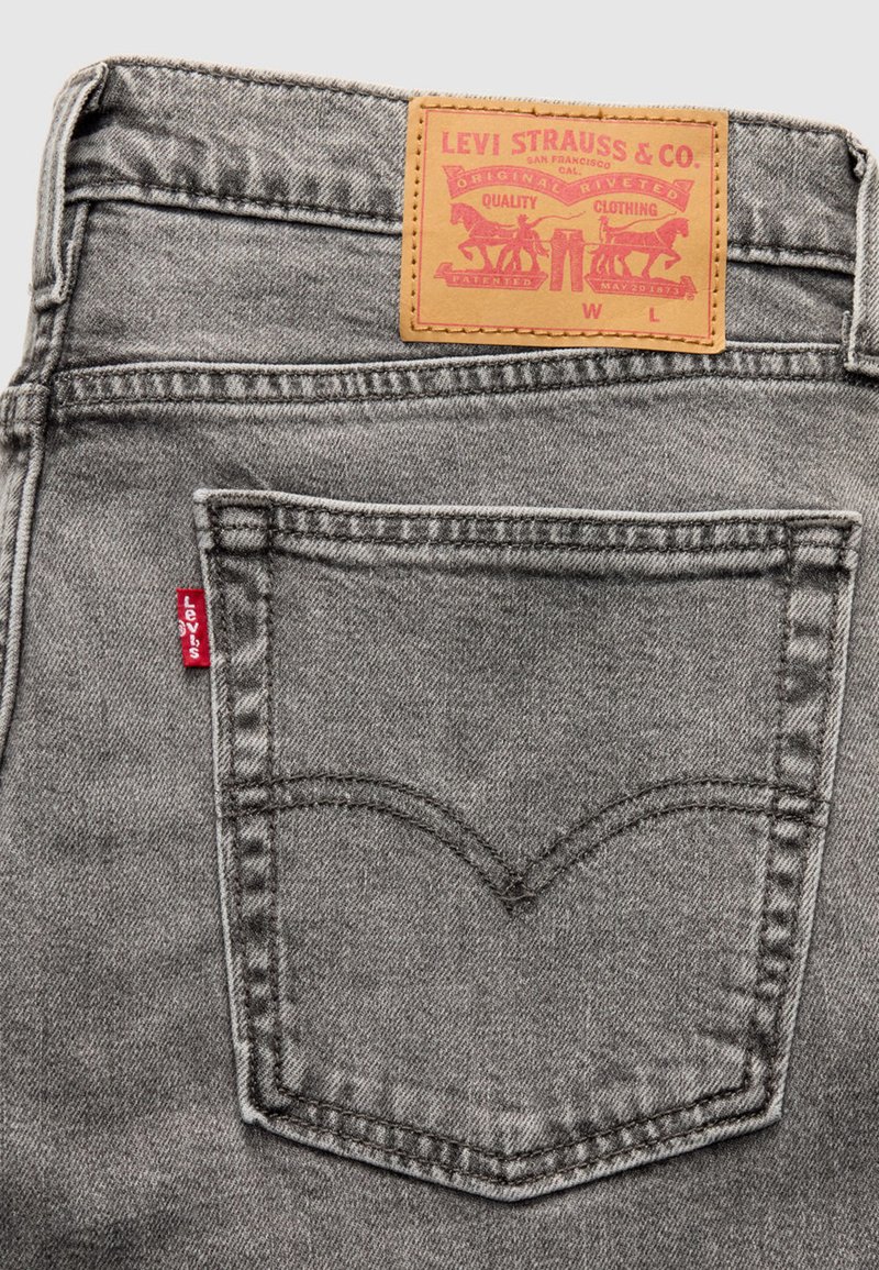 Vaqueros de mezclilla gris con un parche de cuero de la marca que presenta el logotipo de Levi's y un diseño de herradura. Detalle de pestaña roja en el bolsillo trasero.