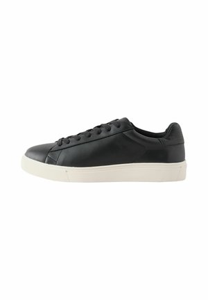 Zwarte lage leren sneaker met zwarte veters en dikke witte rubberen zool, getoond van de buitenkant op een witte achtergrond.