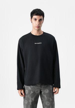 Schwarzes Longsleeve-Shirt mit rundem Halsausschnitt und weißem "marimekko"-Logo, kombiniert mit grauen, floral gemusterten Hosen aus Baumwollstoff.