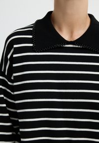 Maglione a righe bianche e nere con colletto a contrasto decorato con perline nere, che presenta un motivo di maglia testurizzata.