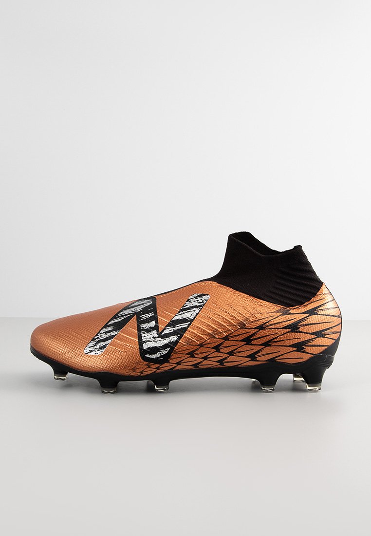 Chaussure de football orange avec une tige texturée, un col en chaussette noir et des crampons noirs. Présente un logo noir et blanc proéminent sur le côté.