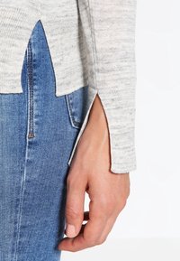 Jasnoszary sweter z dzianiny z bocznymi rozcięciami w połączeniu z niebieskimi dżinsami. Miękka tekstura i luźny krój podkreślające swobodny styl.