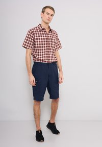 Kortärmad rutiga skjorta i röd och vit med knapplist, tillsammans med marinblå cargoshorts med sidofickor och mörka skor.