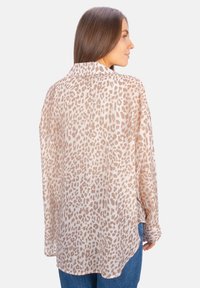 Sheer blouse in light beige with brown leopard print, long sleeves, and a curved hem. Soft texture and relaxed fit.