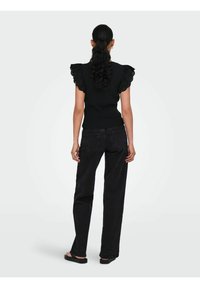 Sort strikket top med dekorative blondeflæser, parret med sorte højtaljede jeans og sorte flade sandaler. Bagview vist.