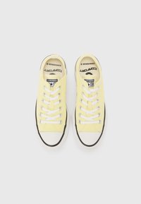 Yellow canvas sneakers with white laces, black rubber sole, and white toe cap. Features logo on tongue and black accents around the sole.