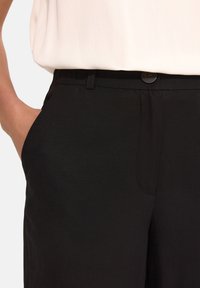Czarne spodnie o gładkiej fakturze, z pasem, zapięciem na guzik i kieszeniami bocznymi. Krój jest dopasowany, z prostymi nogawkami.
