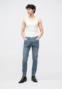 Λευκό ριμπ αμάνικο τοπ, μπλε τζιν παντελόνι από denim και μαύρα δερμάτινα μποτάκια. Τζιν παντελόνι στενής εφαρμογής με πέντε τσέπες, επίπεδη μέση και ελαφρά φθορά.