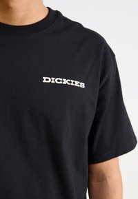 Juodas medvilninis marškinėlis, ant kairiojo krūtinės išspausdinta balta logo "DICKIES". Apvalus iškirpimas ir trumpomis rankovėmis. Lygi tekstūra.