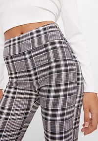 Czarno-białe spodnie w kratę o wysokim stanie z teksturowanym wykończeniem i bocznym zamkiem, dopasowany krój oraz różnorodne wzory pasków.