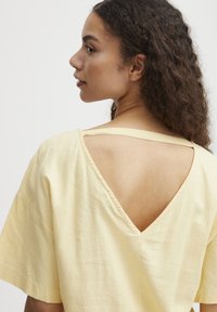 Haut en coton jaune avec un design à dos en V, des manches courtes et une coupe décontractée, avec des coutures visibles le long des bords.