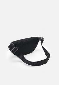 Černá textilní ledvinka s texturovaným logem, zipovým uzávěrem a nastavitelným popruhem s bočním uvolňovacím přezkou. Kulatý tvar s jemnými detaily.