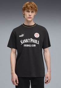 Sort bomulds-t-shirt med korte ærmer, med gule detaljer, Puma-logo og "Sankt Pauli Fussball Club" i hvid tekst.