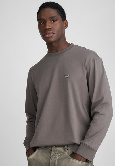 Gray long-sleeve t-shirt with a crew neck and a small embroidered logo on the chest. Soft fabric and relaxed fit, detailed stitching at cuffs.