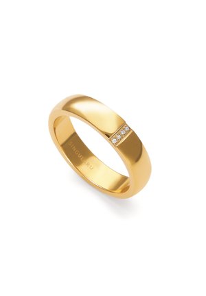 Anillo de banda de oro con cuatro pequeños diamantes colocados en fila sobre la superficie lisa, reflejando la luz sobre un fondo blanco.