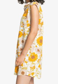 Vestido floral con girasoles en amarillo y naranja sobre un fondo blanco, con cuello y mangas cortas, hecho de una tela ligera.