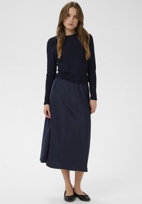 Námornícka blúzka s dlhým rukávom z textúrovanej látky a zodpovedajúca sukňa po členky z hladkého materiálu; nosené s čiernymi plochými topánkami.