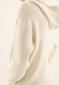 Cremfarbener Rippstrick-Hoodie mit lockerer Passform und weicher Textur. Verfügt über eine Kapuze und raglanärmel für eine bequeme Silhouette.