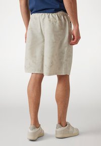 Light beige shorts with a subtle pattern, elastic waistband, and side pockets. Made of lightweight fabric, reaching just above the knees.