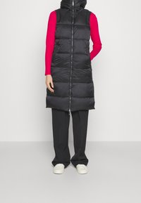 Czarna pikowana kamizelka z zamkiem błyskawicznym, wysokim kołnierzem i bocznymi kieszeniami. Nosi się ją na jasnoczerwonej bluzce z długim rękawem, w połączeniu z czarnymi spodniami.