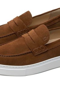 Braune Wildlederloafers mit einer weißen Gummisohle, glatter Textur, kontrastierenden Nähten und einem dekorativen Riemen an der Oberseite.