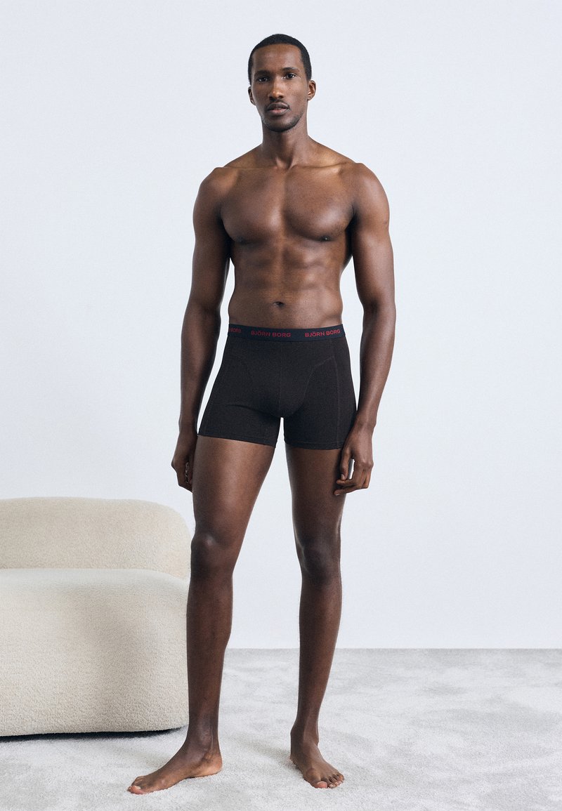 Fekete boxer alsónadrág piros elasztikus derékpánttal, amelyen a "BJÖRN BORG" logó található, sima anyagú textúrával és testhez álló kialakítással.