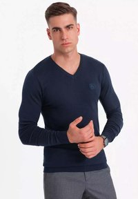Granatowy sweter w serek z miękkiego dzianiny; dopasowany krój, ściągacze na rękawach i u dołu, z dyskretnym logo na piersi.