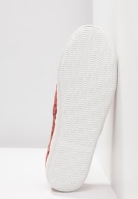 Sko med en struktureret, pink overdel og en hvid, mønstret gummisål, der fremhæver et minimalistisk design og en afrundet tå.