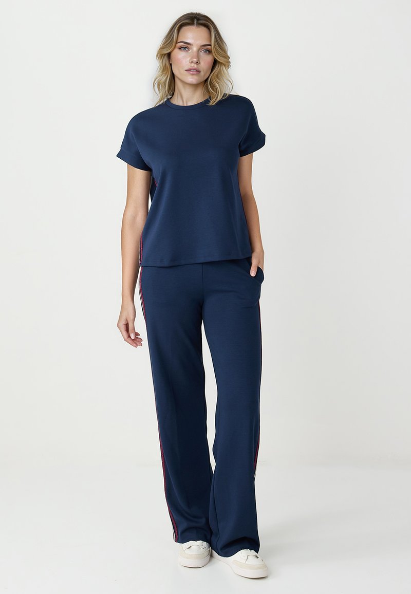 T-shirt en coton bleu marine à manches courtes et coupe décontractée, associé à un pantalon bleu marine assorti avec des bandes latérales rouges et une coupe droite.