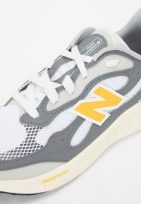 Grå och vit sportskor med mesh-övre, snörning och gult logotyp. Har texturerade överlägg och dämpad sula märkt "FRESH FOAM."