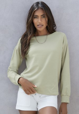 Long-sleeve, light olive green top with a relaxed fit and gathered sleeves, paired with white shorts featuring patch pockets.