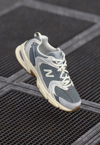 Lightweight running shoe with a mesh upper in gray and navy, featuring white laces, a cushioned sole, and a textured rubber outsole.