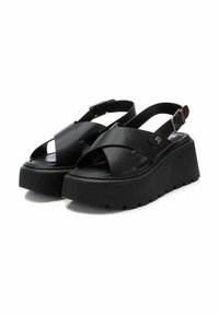 Sandalias de plataforma negras con tiras cruzadas hechas de material sintético suave. Presentan una suela texturizada y una correa para el tobillo ajustable.