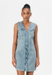 Ermeløs denimkjole i lys blå med V-hals, frontlukking med knapper og sidelommer; har vertikale sømmer og lett utsvingt fald.