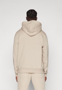 Hoodie bege com capuz ajustável, textura suave, punhos e bainha canelados, usado com calças de treino bege combinando.